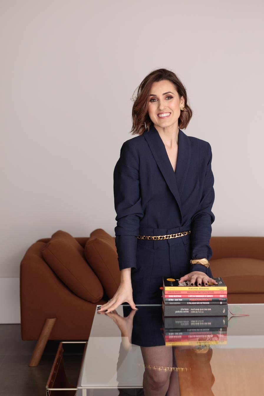 Bruna Maria de Moura ao lado de uma pilha de livros sobre branding e posicionamento